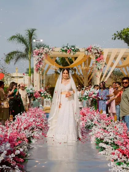 The bride's stunning entrance, walking down an aisle lined with beautiful pink and white blossoms towards the mandap.