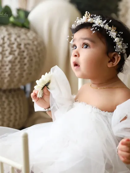 An angelic portrait of a baby girl in a white tulle dress, looking up with a curious expression during her sitter session.