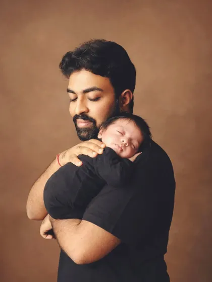 The same loving father and his peaceful baby, captured from a different angle. The warm, earthy background complements the tender mood.