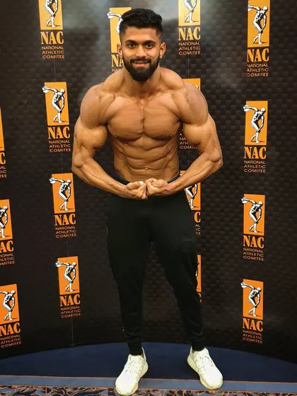 Posing in front of the National Athletic Committee (NAC) banner. This front relaxed pose is the first impression you give the judges, showcasing symmetry and proportion.