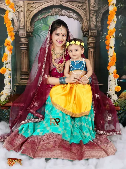 A mother dressed as Yashoda holds her daughter, who is dressed as Radha, on a swing. This beautiful portrait captures a loving moment within a traditional theme.