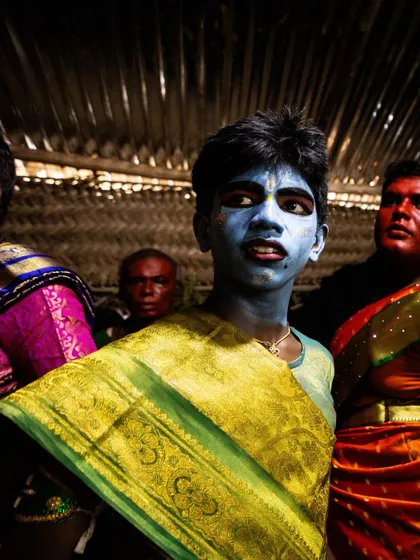 A young participant at the Kulasai festival, his face painted blue, looks away with a thoughtful expression. It shows the human side behind the divine mask.