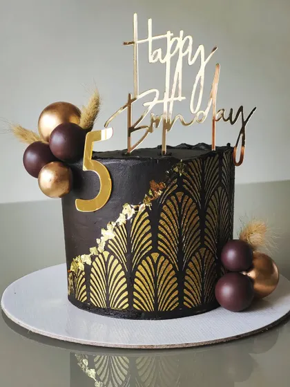 A sophisticated black and gold birthday cake. The design features a dark chocolate buttercream and an elegant art-deco stencil pattern, perfect for a stylish celebration.