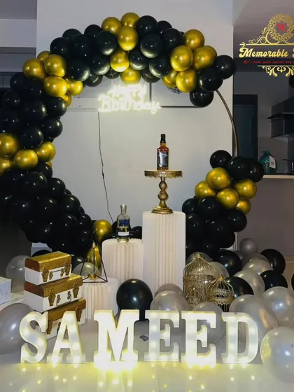 An elegant black and gold balloon ring with marquee letters, perfect for a stylish birthday celebration. A bottle of whiskey on the plinth adds a personalized touch for an adult party.