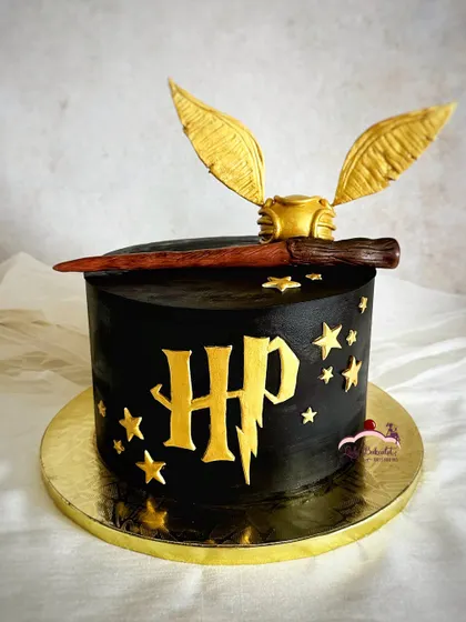 A sleek and minimalist Harry Potter cake. This design features a black ganache finish with the iconic HP logo, stars, and a handcrafted golden snitch and wand on top.
