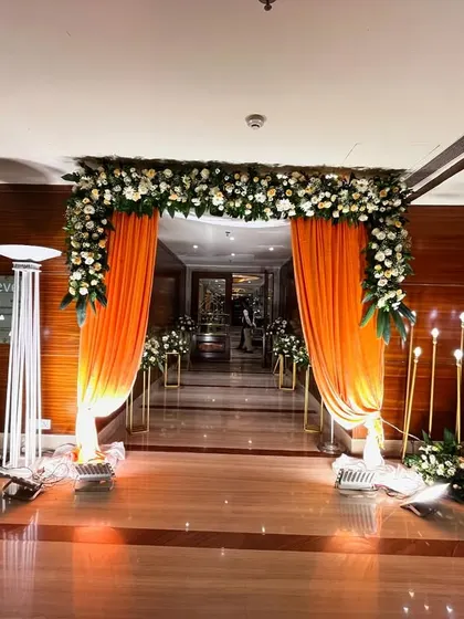 An elegant entrance setup at Jaypee Siddharth. The walkway is lined with tall, candle-like floor lamps, and the doorway is framed with orange drapes and a white floral border.