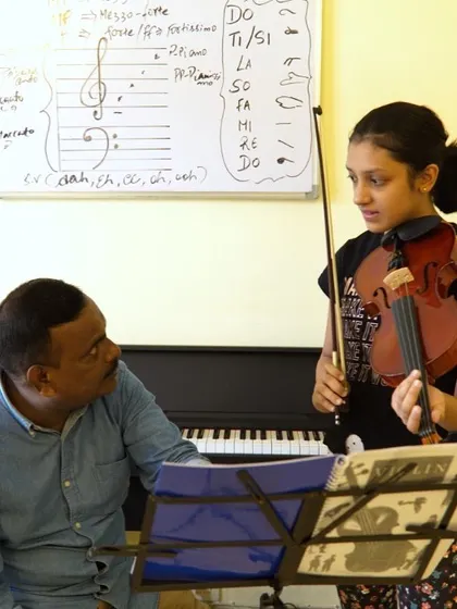In this violin lesson, I am guiding a student through music theory concepts written on the whiteboard, including clefs and solfege hand signs. I integrate theory directly into practical lessons for all instruments to ensure a comprehensive understanding.