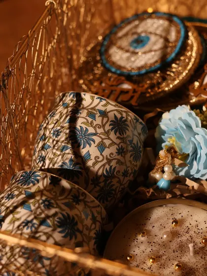 This blue-themed Diwali hamper in a golden basket is filled with block-printed ceramic tumblers and a hand-poured candle, perfect for a sophisticated festive gift.