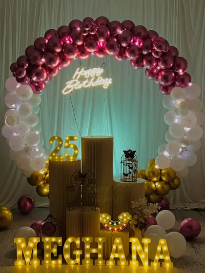 A brightly lit version of the 25th birthday setup for Meghana. This shows how the decoration looks with full lighting, highlighting the chrome balloons and props.