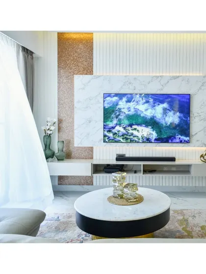 A minimal and modern TV unit design, where a marble feature wall is flanked by a rose gold textured panel and a vertically fluted panel, creating a sophisticated entertainment space.