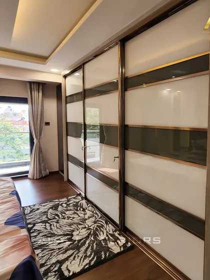A large sliding wardrobe with white and grey glass panels and a metallic frame. The design is modern and sleek, providing ample storage while enhancing the room's aesthetic.