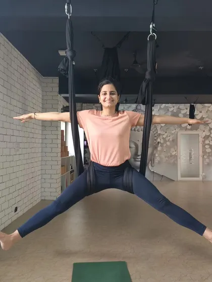 A smiling student enjoys the feeling of flight in a wide-legged aerial pose. Our classes are a space to challenge yourself and find joy in movement.
