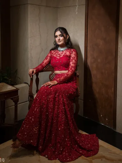 A regal portrait of the bride seated in a vintage chair, her red Sangeet gown flowing around her.