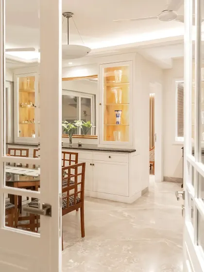 Stepping into the all-white dining area of this cozy apartment. The space features white cabinetry with integrated lighting, providing a clean and timeless backdrop for the wooden dining set.