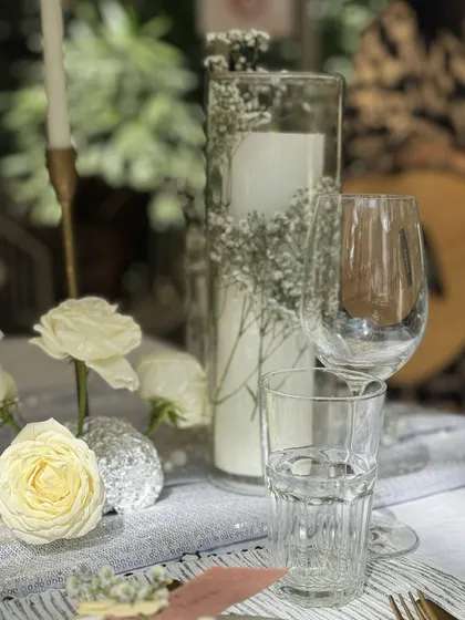 A detail shot of the elegant tablescape, focusing on the interplay of glassware, candles, and fresh white roses, creating a serene and beautiful composition.