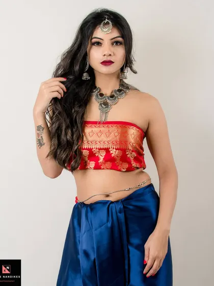 A direct and confident portrait of a model in an ethnic-inspired outfit. The combination of a red brocade top, blue silk skirt, and heavy silver jewelry creates a look that is both divine and powerful.