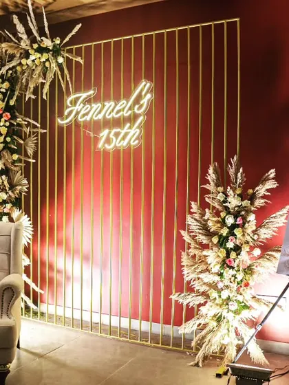 A stylish photo corner for the brand anniversary, featuring a comfortable armchair, a modern gold-grid backdrop, and elegant floral arrangements.