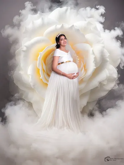 An ethereal portrait of a mom-to-be in a flowing white gown, surrounded by a giant white rose and a cloud of soft smoke for a truly heavenly look.