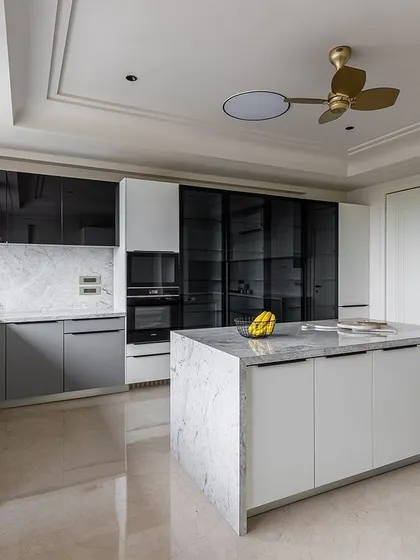 This view showcases the combination of solid, glass, and open-front cabinets, providing a mix of concealed storage and display space. The island is topped with a waterfall granite counter.