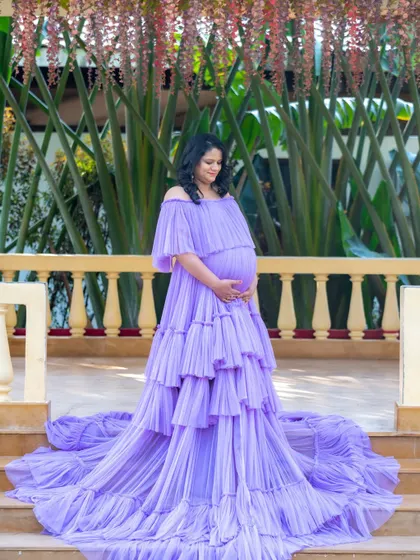 A beautiful portrait of a mom-to-be in a lavender gown, standing on a veranda with hanging flowers.