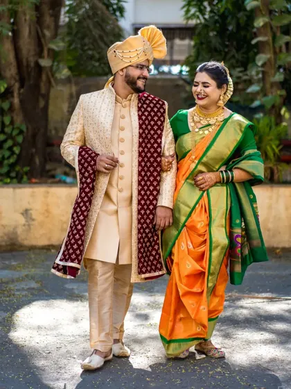 A full-length portrait of the couple walking together, showcasing the groom's sherwani and the bride's traditional Nauvari saree.
