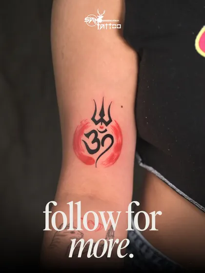 A spiritual symbol with a modern, artistic flair. This tattoo features the classic Om and Trishul symbols, enhanced by a vibrant red watercolor background that adds a dynamic, abstract quality.