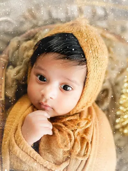 A close-up of a newborn nestled in a basket with golden Christmas ornaments. The warm tones and soft focus create a dreamy, festive mood.