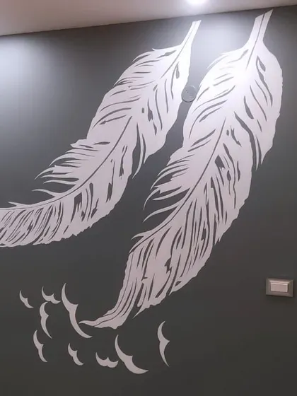 A simple yet elegant stencil of two large white feathers against a dark grey wall. This minimalist design adds a soft and sophisticated touch.