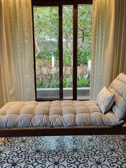 A comfortable chaise lounge I placed by the window in the Alibaug villa. The plush, tufted cushion and patterned floor create a perfect nook for reading and enjoying the garden view.