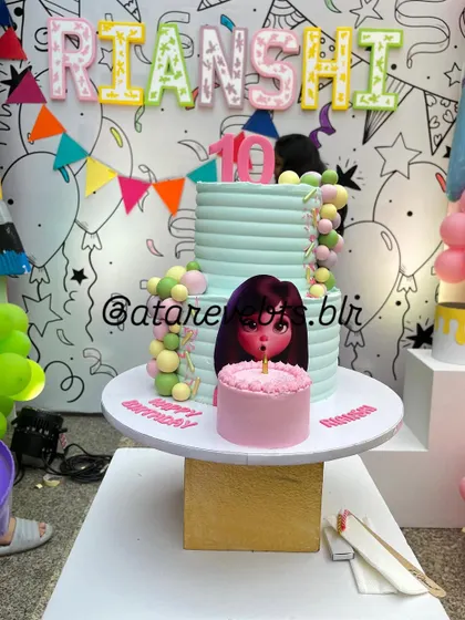 The birthday cake for an art-themed party. The cake is a two-tiered creation with a mini-cake on top, set against a backdrop of a custom-drawn wall, perfectly fitting the creative theme.