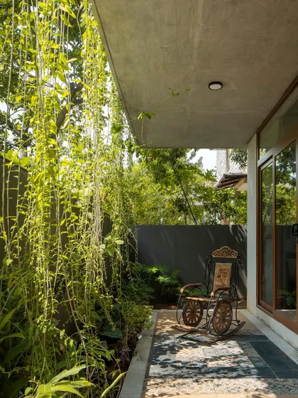 Even smaller, transitional spaces are designed to connect with nature. This covered side passage features a traditional rocking chair next to a curtain of hanging vines, creating a peaceful corner for reflection.