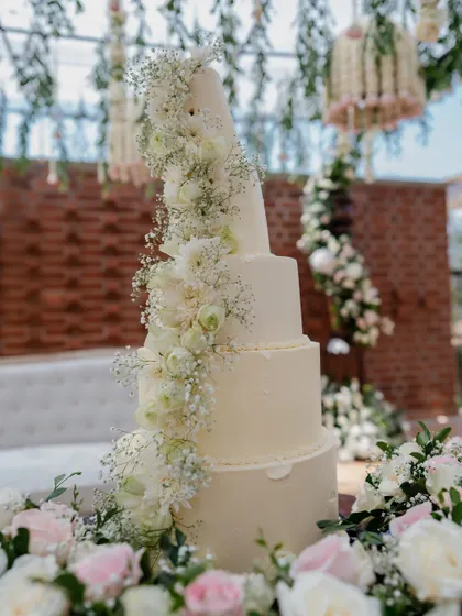 A stunning multi-tiered wedding cake adorned with a cascade of fresh white flowers. The cake is designed to be a centerpiece that perfectly matches the event's elegant white and green floral theme.
