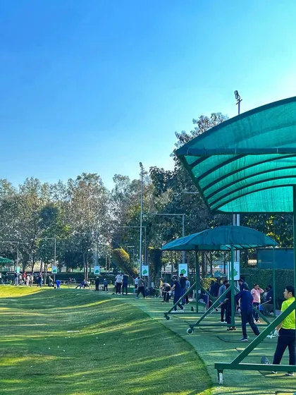 A wide shot of the driving range on a sunny day, showing the green canopies and the lush fairway.