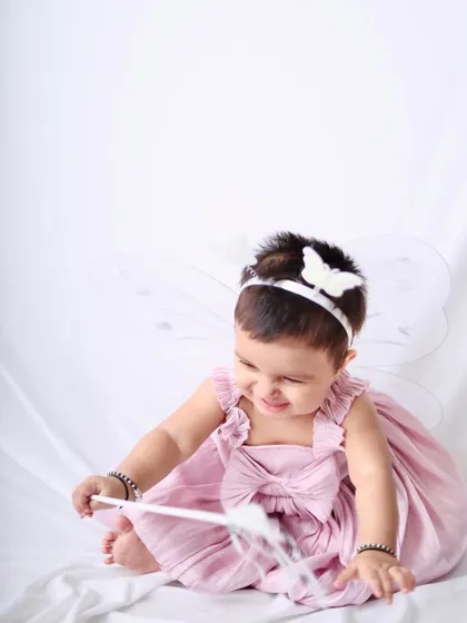 A playful shot of the little fairy girl smiling as she plays with her magic wand against a simple white background.