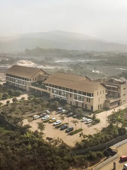 An aerial view showing the JSW Sanjeevani Hospital integrated into the industrial and rural landscape of Dolvi. The building's form and materials are chosen to be in harmony with the local context, making it a landmark for the community.