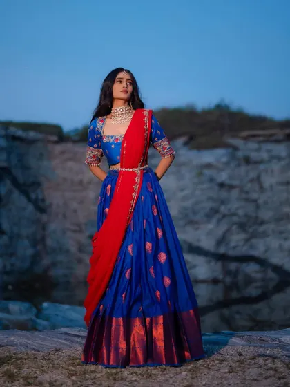 A full-length view of the royal blue and red half saree, showcasing its majestic and elegant silhouette against a dramatic backdrop.