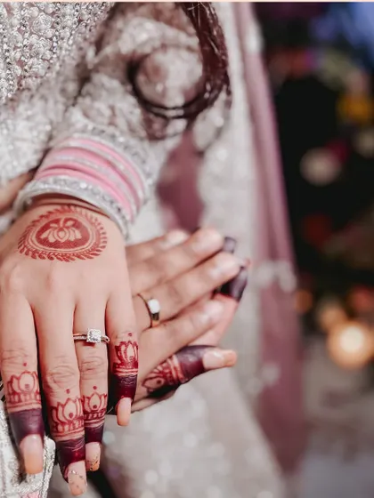 A detailed shot of the couple's hands, showcasing the engagement rings and the bride's intricate henna design.