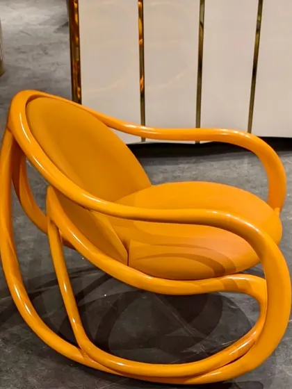A modern interpretation of our rocking chair, finished in a vibrant, high-gloss orange lacquer. This piece adds a playful and bold pop of color to any space.