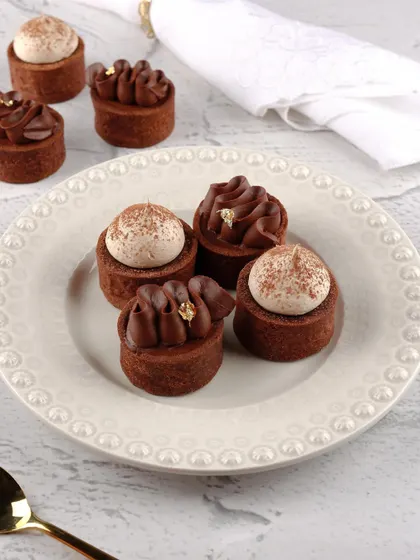 Tiny chocolate tarts with intricate piping and gold leaf details, shot to look elegant and luxurious.