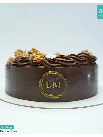 A profile shot of the Chocolate Almond Nougatine cake, emphasizing the rich chocolate collar and the golden 'LM' seal.