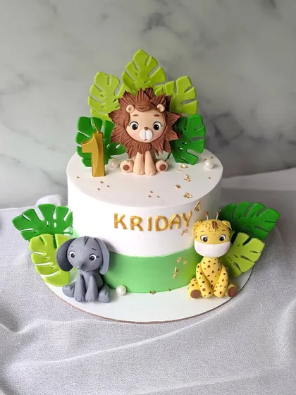 A sweet and simple jungle theme cake for a first birthday. This cake features a cute lion, elephant, and giraffe surrounded by tropical leaves.
