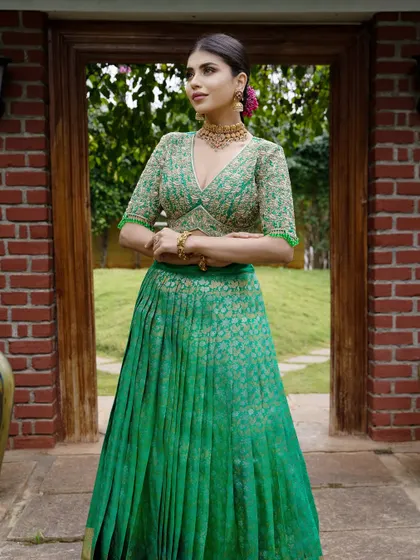 A full view of a rich green Kanchipuram silk half saree, designed for a bridal collection. The deep V-neck blouse is heavily embroidered, creating a look of modern romance and timeless elegance.