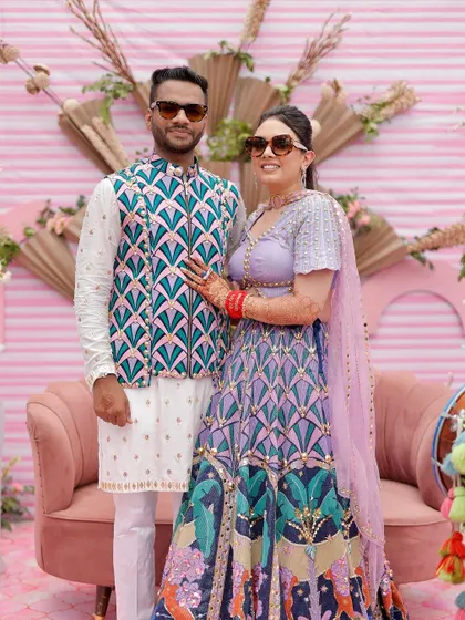 A fun and stylish couple portrait from a quirky pink Mehendi. The backdrop features dried palm fans and modern sculptural elements for a contemporary look.