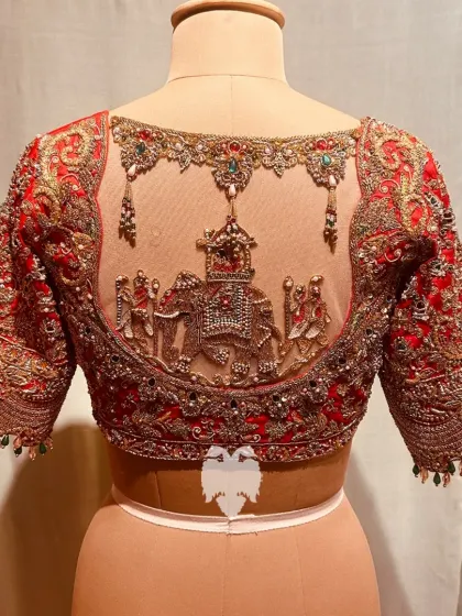 For an auspicious Muhurtham, this red silk blouse features a net back showcasing a traditional 'baradh' concept of an elephant procession.