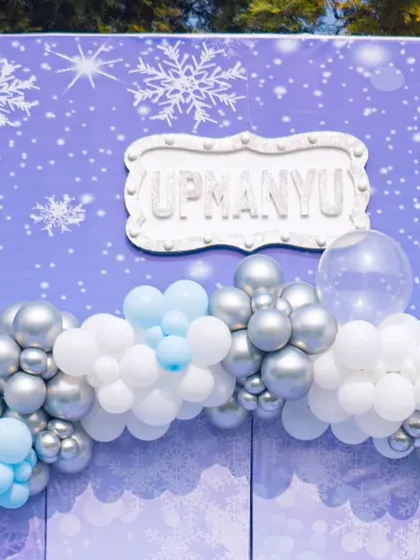 A personalized name plaque for the birthday boy, set against the snowy backdrop and framed by a silver and blue balloon garland.