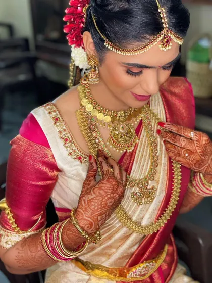 This bride is adjusting her stunning temple jewelry. The makeup is designed to harmonize with the traditional gold accessories, featuring a clean base and soft eye makeup.
