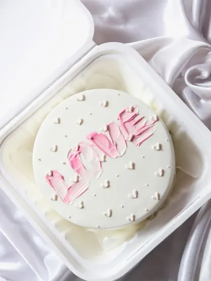 A trendy bento cake with 'LOVE' written in a pink brushstroke effect, surrounded by tiny hearts.