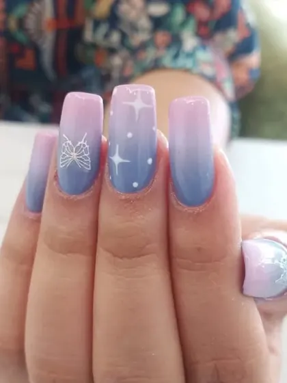 A celestial-themed design on square-shaped nails. This set features a pink and blue ombré base with hand-painted stars and a butterfly.