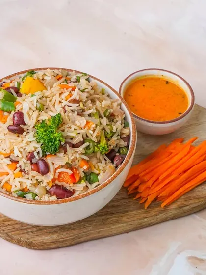 A light and healthy vegetable rice bowl with kidney beans, served on a wooden platter against a bright background.