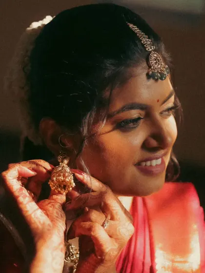 A close-up of a bride adjusting her jhumka. The warm, soft lighting and her gentle smile make this a sweet and intimate getting-ready photo, full of happy anticipation.